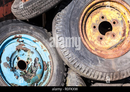 Ein Haufen rostigen alten gelben und blauen Auto, Transporter oder LKW-Räder mit Reifen abgenutzt und schmutzig, in einem Ausschuss oder Junk Yard Stockfoto