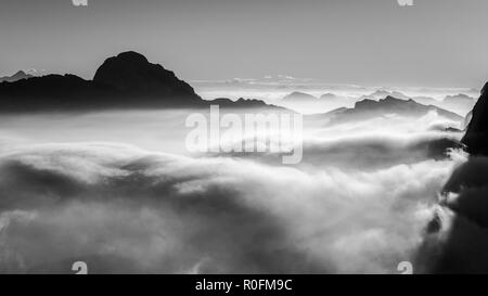 Sich bewegende Wolken über dem Tal bei Sonnenaufgang. Stimmungsvolle Wolkenflut. Schwarz-weiße Berglandschaft. Die Dolomiten. Italienische Alpen. Europa. Stockfoto