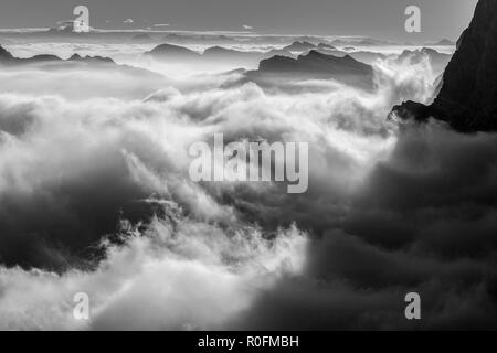 Sich bewegende Wolken über dem Tal bei Sonnenaufgang. Stimmungsvolle Wolkenflut. Schwarz-weiße Berglandschaft. Die Dolomiten. Italienische Alpen. Europa. Stockfoto