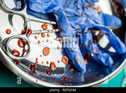 Handschuhe blau und Schere mit Blut befleckt auf einem Tablett in einem Operationssaal, konzeptionelle Bild Stockfoto