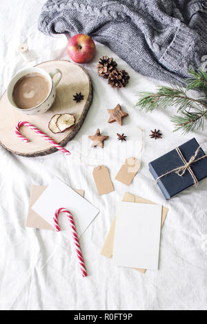 Weihnachten Bett noch leben Komposition. Grußkarten, Geschenkanhänger mockup Szene. Tasse Kaffee, Zuckerstangen, Geschenkbox und Holz- Sterne. Weiße Bettwäsche Bettlaken Hintergrund. Winter Flach, Ansicht von oben. Stockfoto