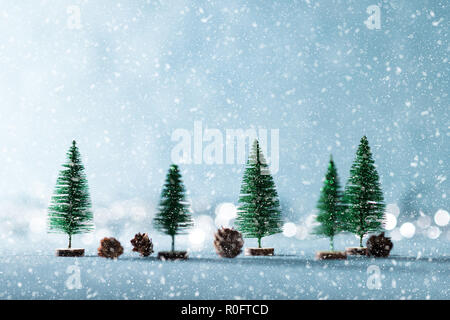 Märchenhaft verschneite Winterlandschaft Hintergrund. Miniatur immergrünen Bäumen und Tannenzapfen auf glänzenden blauen Hintergrund mit Bokeh im Hintergrund. Stockfoto