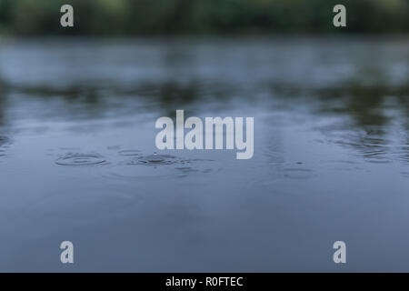 Ruhe Regen fällt auf die Oberfläche des Wassers in eine Pfütze mit abgestuften Schatten der schwarzen Schatten und Reflexionen der blauen Himmel Stockfoto