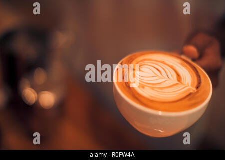 Heiße Kunst latte Kaffee in einer Tasse auf Holztisch und Coffee Shop blur Hintergrund mit bokeh Bild. Latte Art Coffee table top, gerne entspannende Stimmung Stockfoto