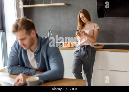 Super Blonde Hausfrau SMS senden, während ihr Freund mit dem Notebook Stockfoto