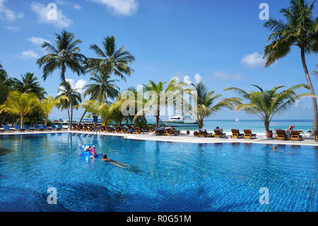 Malediven - Januar 17, 2013: die Menschen schwimmen im Wasser Pool, der von tropischen Meer Strand mit Kokospalmen und Liegestühlen. Die idyllische Landschaft von Seaside r Stockfoto