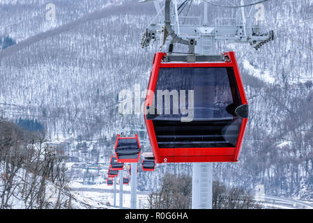 Verschwindende Reihe der roten Seilbahnen lift Kabinen in Krasnaja Poljana Ski Mountain Resort. Gondeln Detailansicht auf verschneiten Berg Hintergrund im Winter Stockfoto