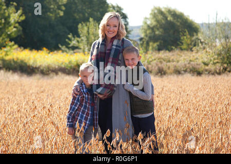 Ein schönes Lächeln Mama legt ihre Arme um ihren zwei süßen Kinder, außerhalb in einem Feld Stockfoto