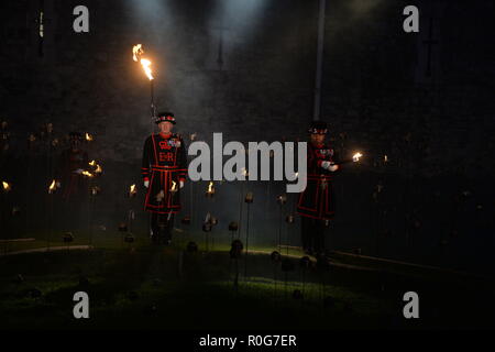 Yeoman Warders ('Beefeaters') zündet die ersten von Tausenden von Flammen in einer Beleuchtungszeremonie im Trockengraben des Tower of London als Teil einer Installation namens Beyond the Vertiefung Shadow: The Tower Remints, um den hundertsten Jahrestag des Endes des Ersten Weltkriegs zu feiern. Stockfoto