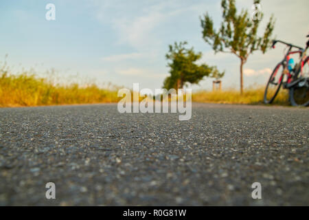 Radweg Asphalt, Pause bei der Radtour am Abend, das Fahrrad an der Kante steht, tiefe Perspektive mit Blick entlang der Route Stockfoto