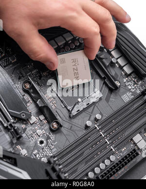 Prozessor Ryzen 7 2700X in der Hand vor dem Hintergrund einer Computerhauptplatine. Stockfoto