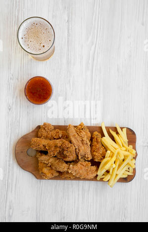 Tasy fast food: Gebratene Hähnchenschenkel, würzige Flügel, Pommes frites und Chicken Strips mit Sauer-süßen Soße und kaltes Bier über weiß Holz- Hintergrund, Ove Stockfoto