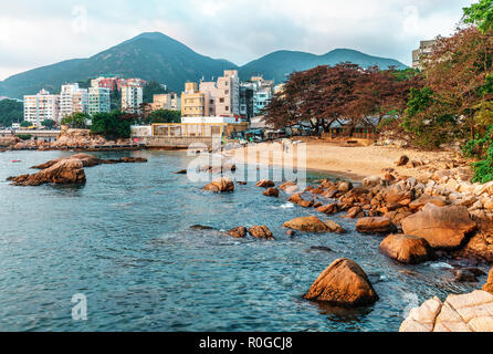 Felsige Küste und kleine Sandstrand von Stanley Bay in Hongkong. Landschaftlich schöne Landschaft mit Wasser, Berge, Felsen und Gebäuden Stockfoto