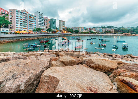 Fischerboote in Stanley Bay in Hongkong, die von felsigen Küste auf Gebäuden Hintergrund. Landschaftlich schöne Landschaft von Stanley waterfront in der selbst Stockfoto