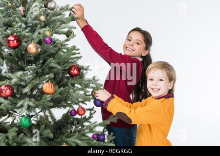 Gerne Geschwister schmücken Weihnachtsbaum mit Glaskugeln isoliert auf weißem Stockfoto