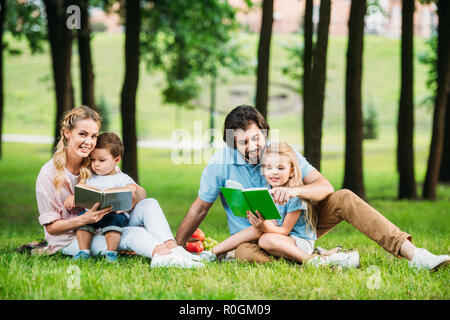 Schöne junge Familie sitzt auf dem Rasen im Park und lesen Bücher Stockfoto