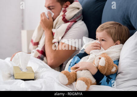 Kranken Vater und Sohn blasen Nasen mit Papierservietten, während im Bett lag, Stockfoto