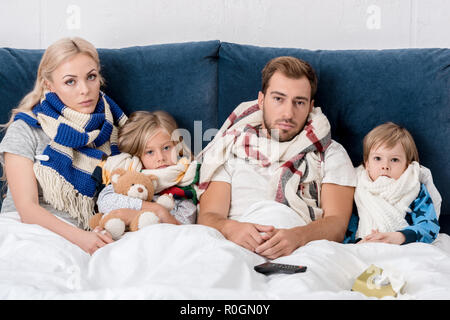 Kranke junge Familie in Schals an Kamera suchen, während im Bett lag, Stockfoto