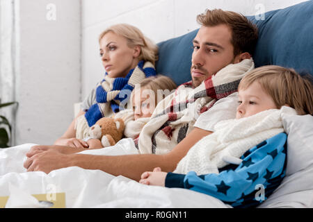 Kranke junge Familie in Schals im Bett lag, zusammen Stockfoto