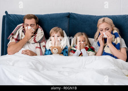 Kranke junge Familie blasen Nasen mit Servietten zusammen, während im Bett lag, Stockfoto