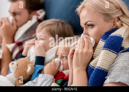 Nahaufnahme der kranke junge Familie blasen Nasen mit Servietten zusammen, während im Bett lag, Stockfoto