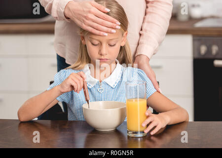 7/8 Schoß von Mutter Kontrolle Töchter Temperatur mit der Hand während Sie frühstücken Stockfoto
