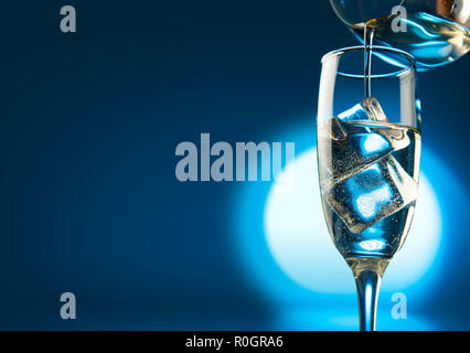Champagner im Glas mit Eiswürfeln über hellen Hintergrund gießen Stockfoto