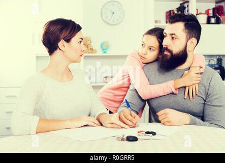 Junger Mann und Frau Unterzeichnung Papiere für Scheidung, während ihre Tochter im Innenbereich Stockfoto