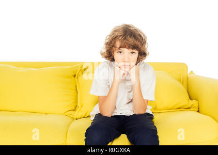 Verärgert Junge sitzt auf der gelben Sofa aufliegt und Kinn auf die Hände isoliert auf Weiss, bei Camera suchen Stockfoto