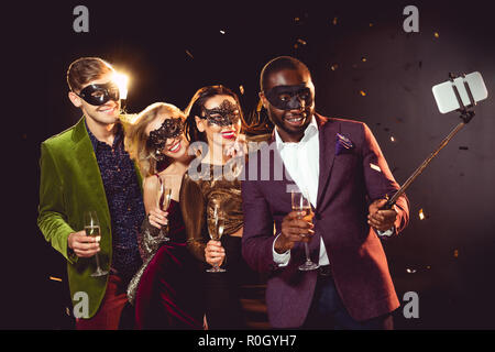 Happy multiethnischen Luxus Paare in Karneval Masken unter selfie auf dem Smartphone Stockfoto