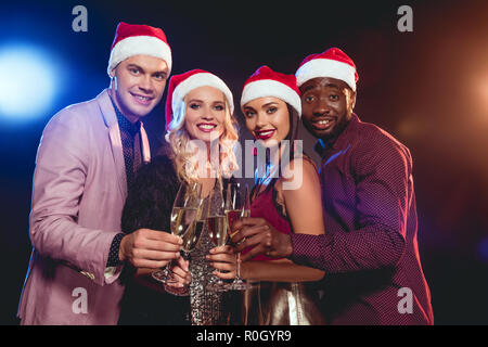 Multikulturelle glamouröse Freunde in santa Hüte klirren Gläser mit Champagner auf das neue Jahr Partei Stockfoto