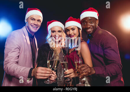 Multikulturelle glamouröse Freunde in santa Hüte klirren Gläser mit Champagner auf das neue Jahr Partei Stockfoto