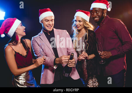 Multikulturelle glamouröse Freunde und Freundinnen in santa Hüte mit Champagner auf das neue Jahr Partei Stockfoto