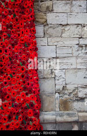 Handgefertigt aus Gewirken und Gestricken Mohnblumen schmücken die Mauer einer Kirche der Hundertjahrfeier der Welt Krieg 1 zugunsten der Poppy Appell zu gedenken. Stockfoto