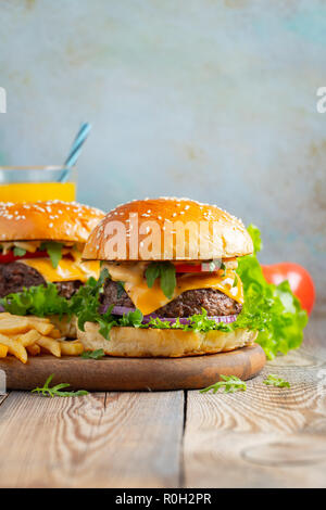 Zwei frische hausgemachte Burger mit Bratkartoffeln und Orangensaft auf einem Holztisch. Mit kopieren. Stockfoto
