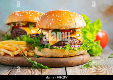 Zwei frische hausgemachte Burger mit Bratkartoffeln auf einem Holztisch. Stockfoto