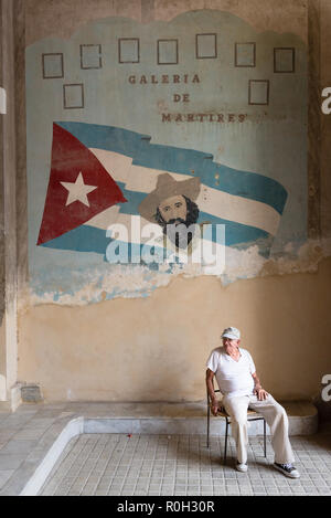 Mann vor Tribut zu Helden der Kubanischen Revolution auf einer Wand in einem Apartment in Havanna Gebäude sitzen Stockfoto