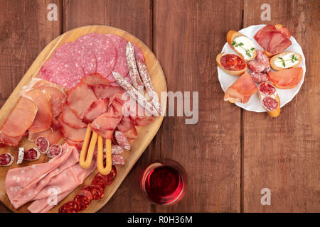 Charcuterie Verkostung. Ein Foto von vielen verschiedenen Wurst und Schinken, Aufschnitt, geschossen von oben auf einem dunklen Hintergrund im Landhausstil mit Rotwein Stockfoto