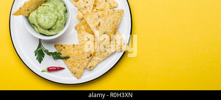Traditionelle lateinamerikanische Guacamole mit Mais Chips, Nachos auf gelben Hintergrund. Banner Format. Stockfoto