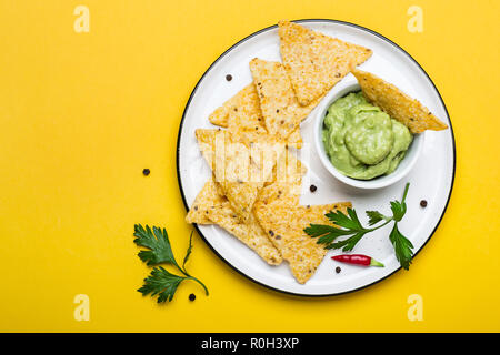 Traditionelle lateinamerikanische Guacamole mit Mais Chips, Nachos auf gelben Hintergrund. Stockfoto
