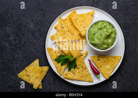 Traditionelle lateinamerikanische Guacamole mit Mais Chips, Nachos auf schwarzem Hintergrund. Stockfoto