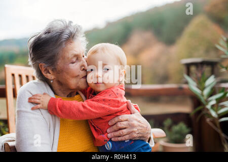 Ältere Frau küssen ein Kleinkind Urenkel auf einer Terrasse im Herbst. Stockfoto