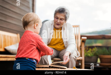 Ältere Frau mit einem Kleinkind Urenkel auf einer Terrasse im Herbst. Stockfoto