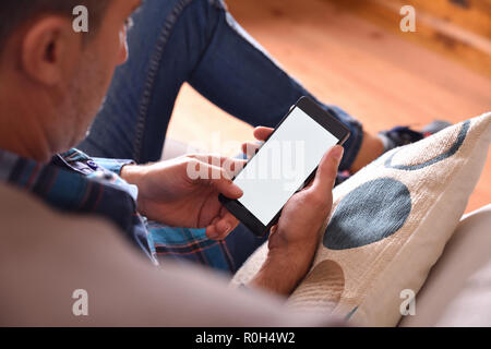 Erwachsenen Mann mit blauem Hemd und Jeans sitzt auf einem mit einem Smartphone Sofa. Aussichtspunkt angehoben Stockfoto