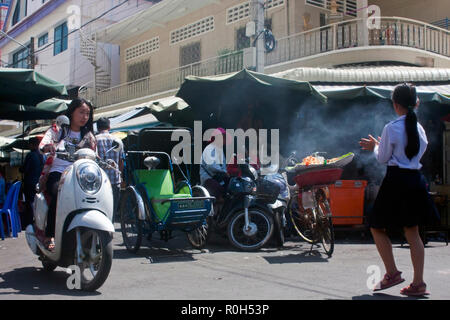 Leute führen ein rauchiges Essen Verkäufer an einer Kreuzung einer belebten Seitenstraße im Zentrum von Phnom Penh, Kambodscha. Stockfoto