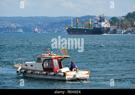 Großes Frachtschiff geht entlang dem Bosporus, ein kleines Fischerboot mit einem Fischer in den Vordergrund. Stockfoto