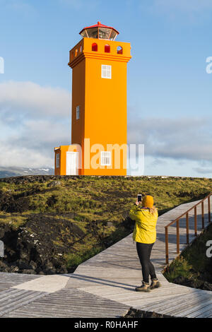 SNAEFELLSNES, ISLAND - August 2018: Frau im gelben Regenmantel, Bild von Svortuloft Leuchtturm. Vertikale Ausrichtung. Stockfoto