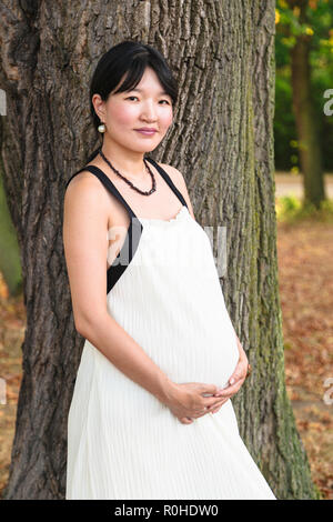 Junge schwangere Frau lächelnd in der Nähe von Tree in Park Stockfoto