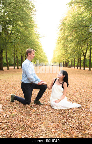 Mann kniet vor seiner Freundin und Heiratsantrag in Park Stockfoto