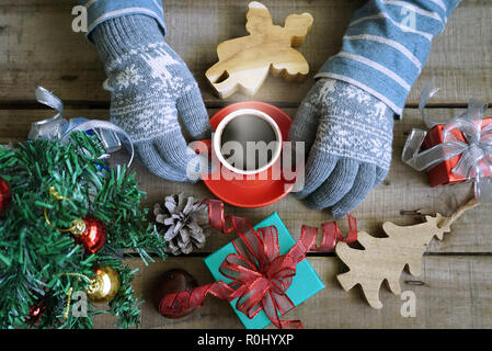 Topview touristische tragen Sie Handschuhe und heißen Kaffee Tasse auf Holz Tisch, die Geschenke Weihnachten Thema dekorieren halten Stockfoto